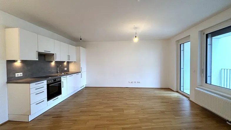 Heller offener Wohn- und Essbereich mit integrierter Küche und Zugang zum Balkon.