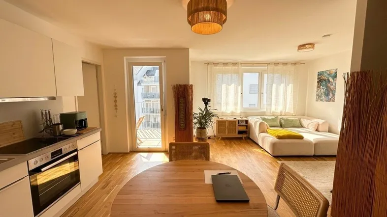 Heller offener Wohn- und Essbereich mit integrierter Küche und Zugang zum Balkon.