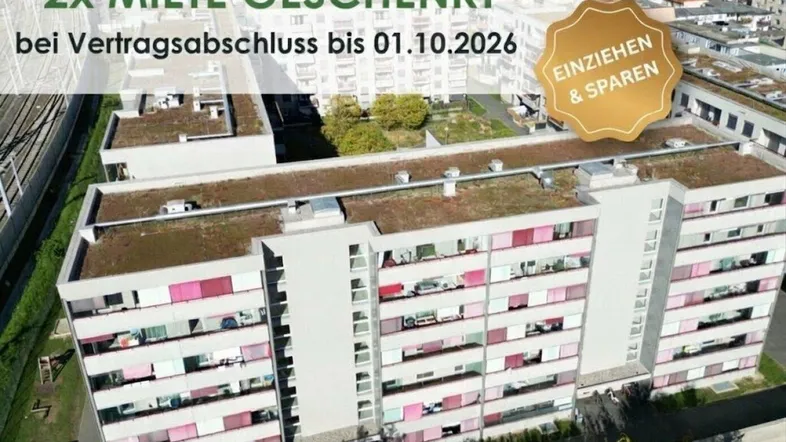 Luftaufnahme eines modernen Mehrfamilienhauses mit Flachdach, grünen Dächern und Balkonen in städtischer Umgebung.