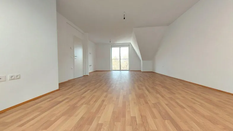Heller, leerer Raum mit Laminatboden, weißen Wänden und Zugang zu einem Balkon oder einer Terrasse.