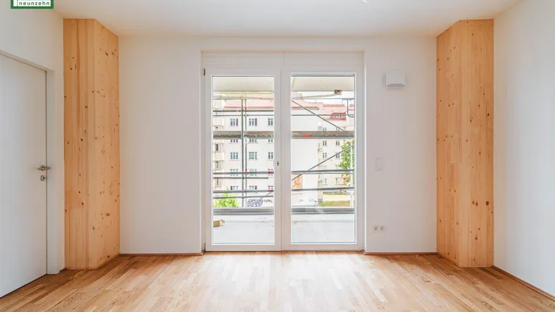 Helles, leeres Zimmer mit Holzboden und Zugang zu einem Balkon oder einer Terrasse, ideal für individuelle Gestaltung.