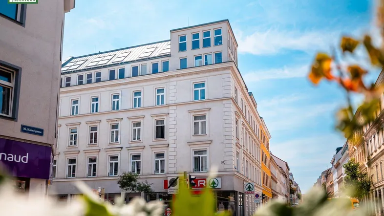 Modernes Mehrfamilienhaus mit Geschäften im Erdgeschoss und vielen Fenstern in einer städtischen Umgebung.