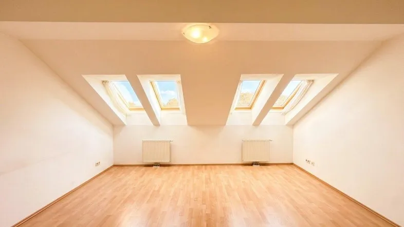 Helles Dachzimmer mit Holzboden und mehreren Dachfenstern, ideal als Wohn- oder Schlafbereich.