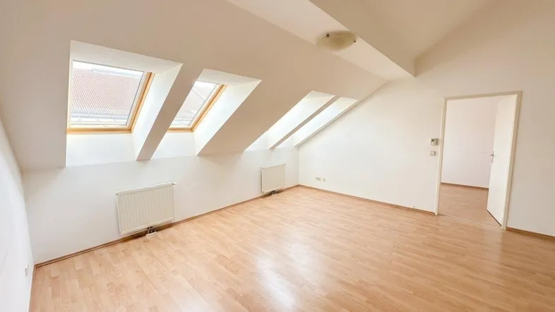 Helles Dachgeschosszimmer mit Schrägdecken und mehreren Dachfenstern, ideal als Wohn- oder Schlafbereich.