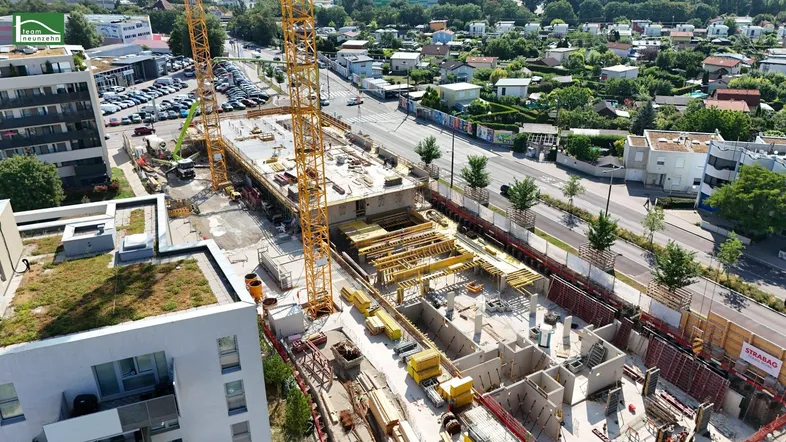 Luftaufnahme einer Baustelle mit Kränen und umliegenden modernen Gebäuden in städtischer Umgebung.