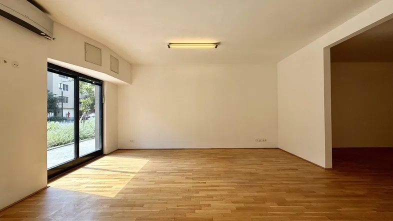 Heller Gewerberaum mit Holzboden, großen Fenstern und Klimaanlage, durchflutet von natürlichem Licht.