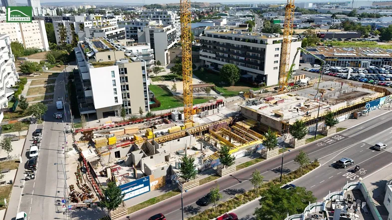 Luftaufnahme einer Baustelle mit Kränen und umliegenden Wohngebäuden in einer städtischen Umgebung.