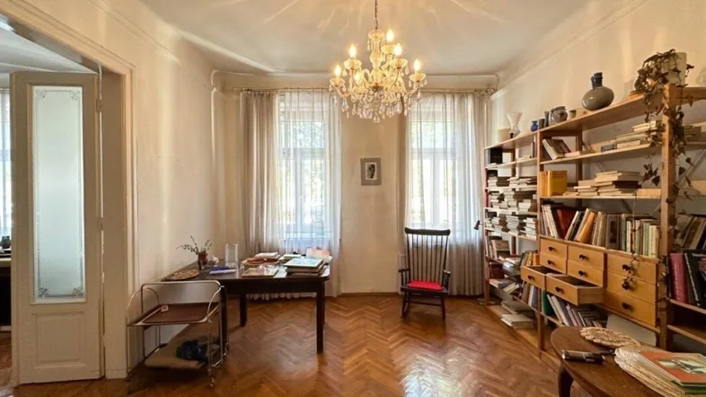 Geräumiges Wohnzimmer mit elegantem Fischgrätparkett, Stuckdecke, Kronleuchter und Bücherregalen.