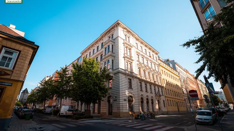 Historisches Eckgebäude mit reich verzierter Fassade an einer belebten Stadtstraße.