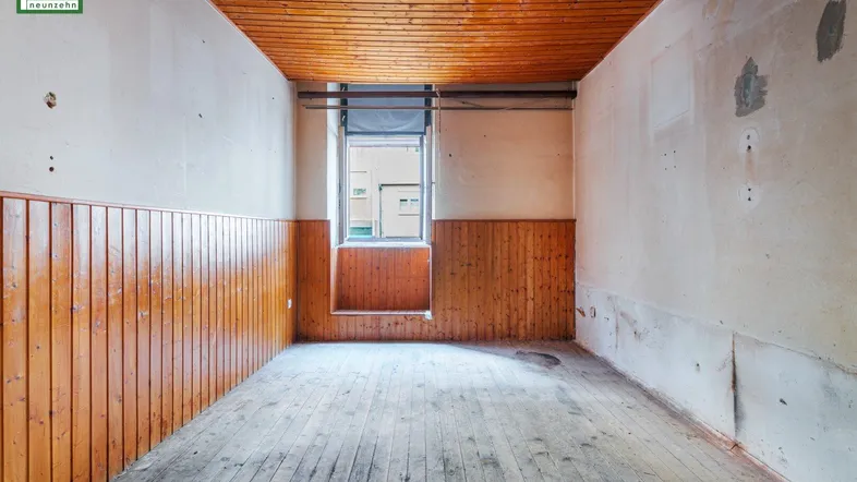Leerer Raum mit Holzvertäfelung, Holzboden und einem Fenster, bereit für Renovierung.