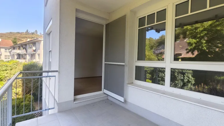 Sonniger Balkon mit Fliesenboden und Zugang zu einem Innenraum, umgeben von viel Grün.