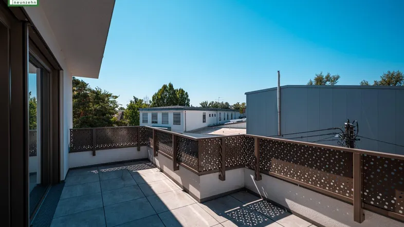 Geräumige Terrasse mit Fliesenboden und moderner Lochblech-Brüstung, umgeben von anderen Gebäuden.