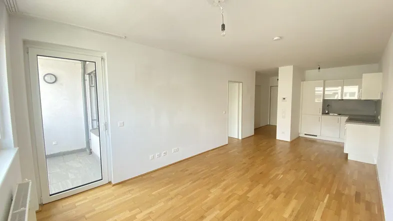 Helles Wohn- und Esszimmer mit offener Küche und Zugang zu einem Balkon.