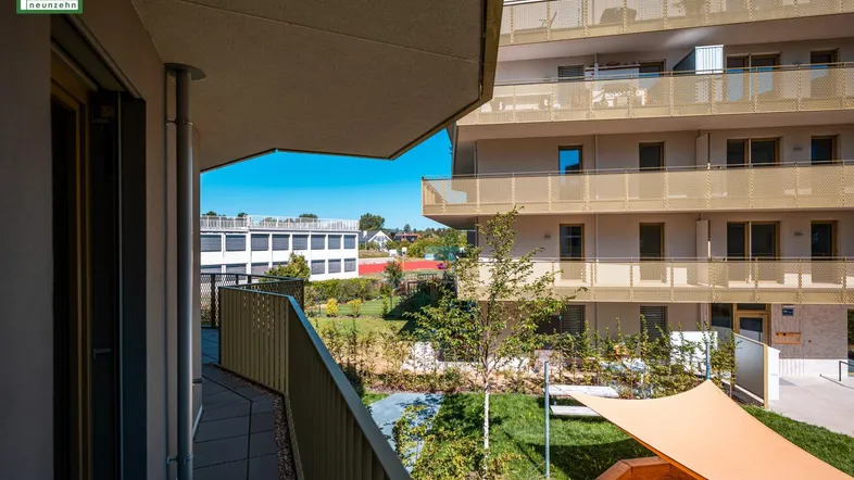 Heller Balkon mit Blick auf den gepflegten Gemeinschaftsgarten und die moderne Architektur des Gebäudes.