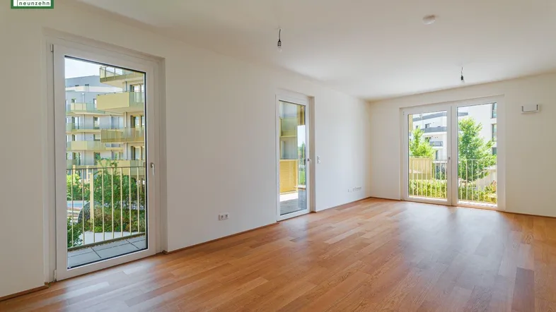 Helles Wohnzimmer mit Holzboden und Zugang zu zwei Balkonen, Blick auf moderne Gebäude.