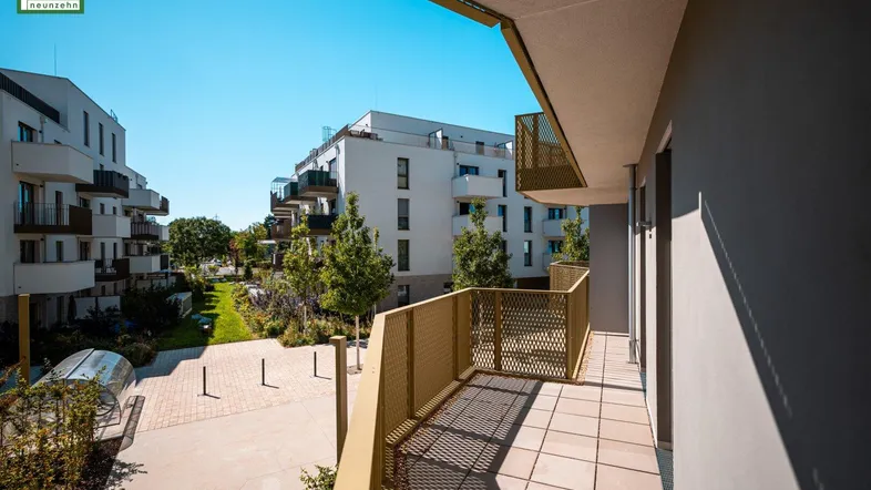 Breiter Balkon mit Fliesen und modernem Geländer, mit Blick auf den begrünten Innenhof und Neubauten.