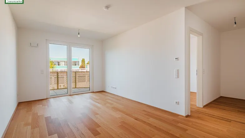 Helles, leeres Zimmer mit Holzboden und Zugang zu einem Balkon, ideal als Wohnbereich.