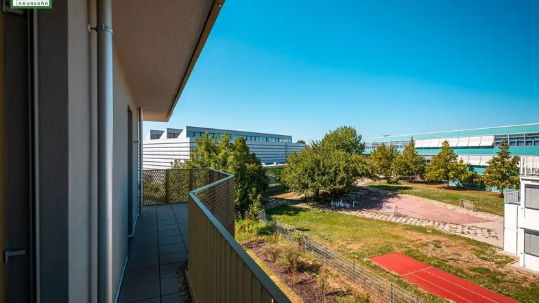 Heller Balkon mit Ausblick auf eine gepflegte Grünfläche und die moderne Wohnbebauung.
