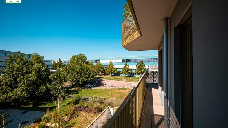 Heller Balkon mit Ausblick auf die grüne Umgebung und die umliegenden Gebäude.