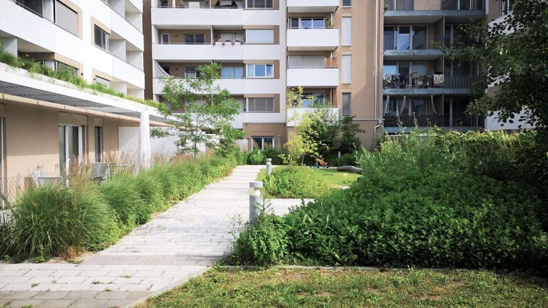 Moderne Wohngebäude umgeben einen begrünten Innenhof mit Wegen und Pflanzen.
