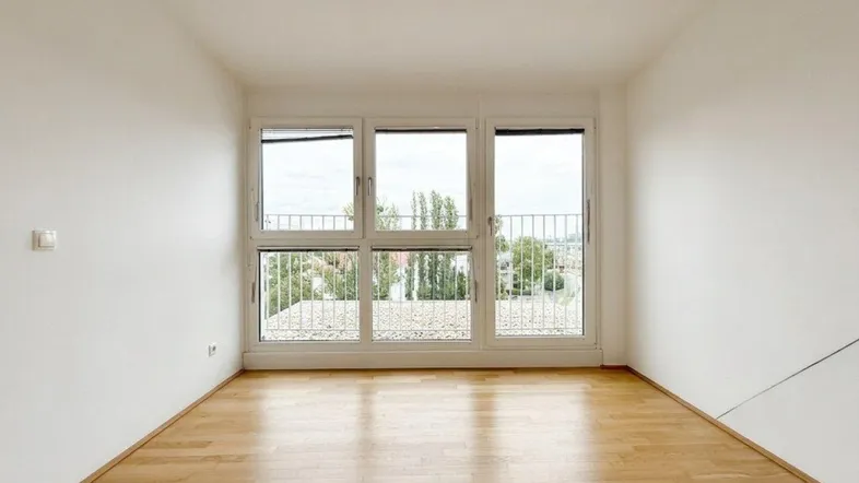 Helles, leeres Zimmer mit großen Fenstern und Blick ins Grüne, ideal als Wohnbereich.