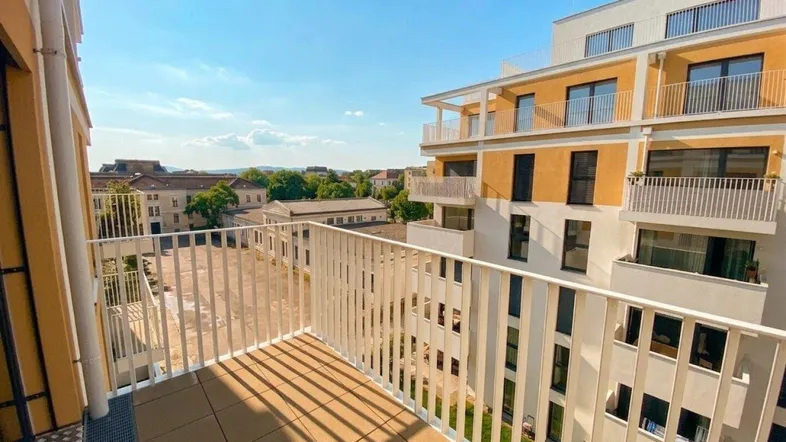 Heller Balkon mit Fliesenboden und Blick auf moderne Gebäude unter blauem Himmel.