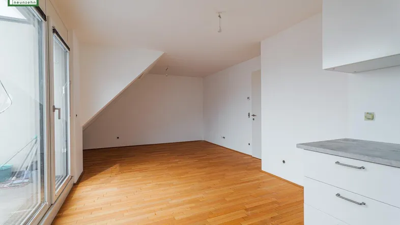 Heller Raum mit Holzboden, Dachschräge und Zugang zu einem Balkon, ideal für Wohn- oder Schlafbereich.