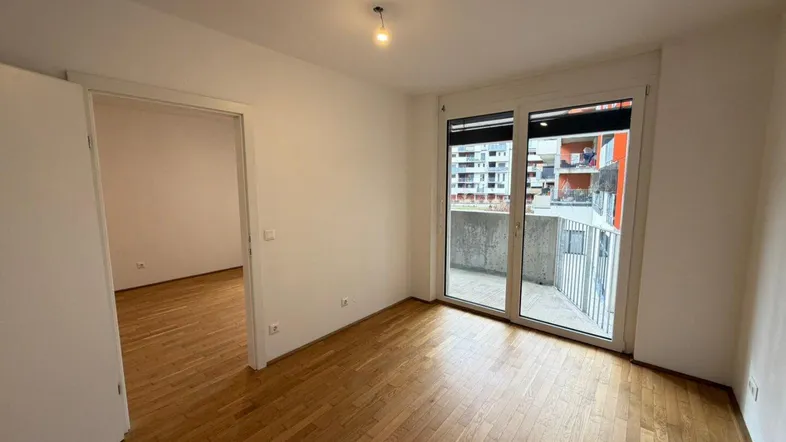 Helles Zimmer mit Parkettboden und Zugang zu einem Balkon, ideal als Schlafzimmer nutzbar.