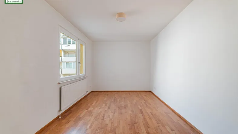 Helles Zimmer mit Parkettboden und Blick auf die umliegenden Gebäude.
