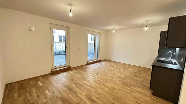 Heller offener Wohn-Essbereich mit Holzboden und Zugang zu zwei Balkonen oder Terrassen.