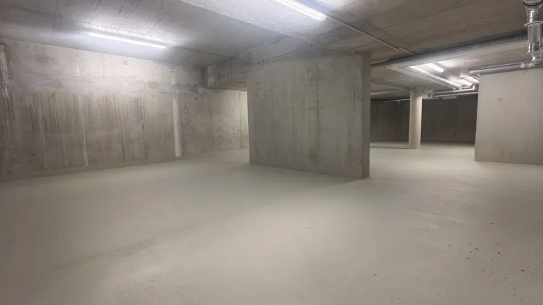 Unfertiger Betonraum mit sichtbaren Rohren und Leuchtstofflampen, geeignet als Lagerfläche.