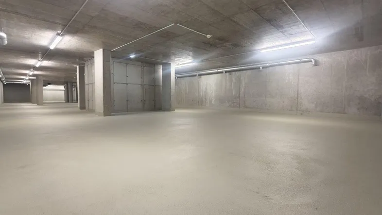 Großer, leerer Raum im Untergeschoss mit Betonwänden und -decke, beleuchtet mit Leuchtstoffröhren.