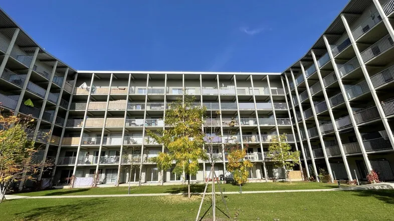 Modernes Wohngebäude mit vielen Balkonen und einem begrünten Innenhof unter blauem Himmel.
