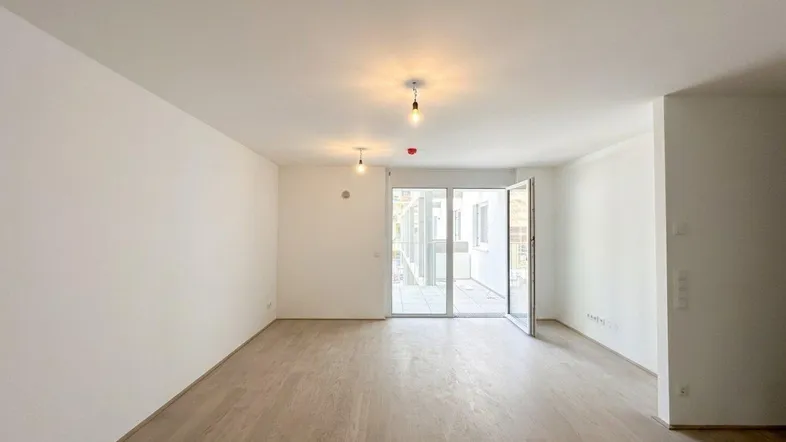 Helles, unmöbliertes Wohnzimmer mit Holzboden und Zugang zu einem Außenbereich.