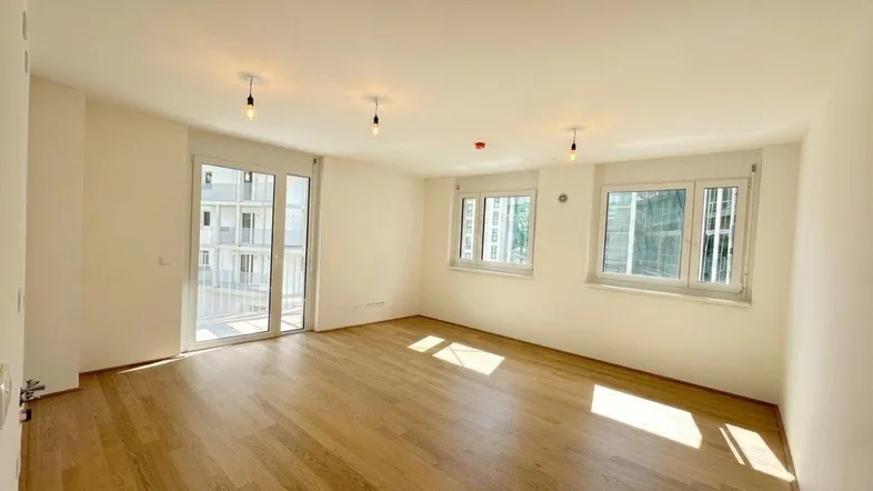 Helles Wohnzimmer mit Holzboden, großen Fenstern und Zugang zu einem Balkon.