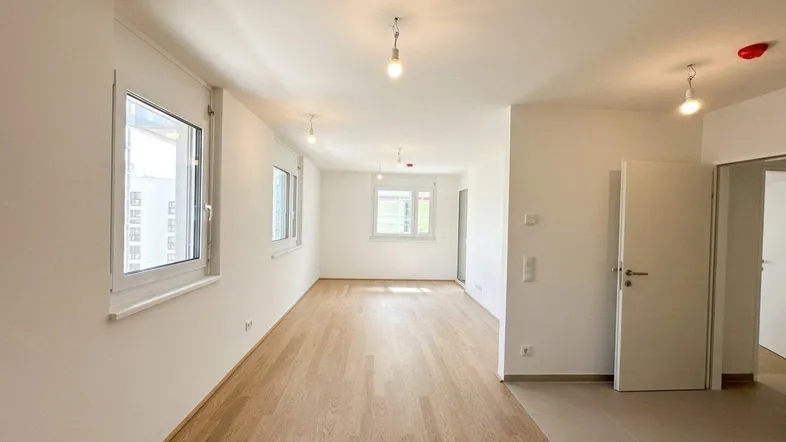 Helles, leeres Zimmer mit Parkettboden und mehreren Fenstern, bereit zur individuellen Gestaltung.