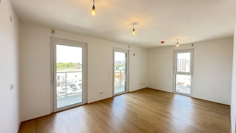 Helles Zimmer mit Holzboden und Zugang zu mehreren Balkonen oder Fenstern, ideal für Wohn- oder Schlafbereich.