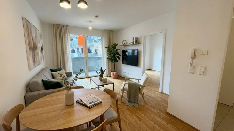 Helles Wohn- und Esszimmer mit Holzboden, moderner Einrichtung und Zugang zum Balkon.