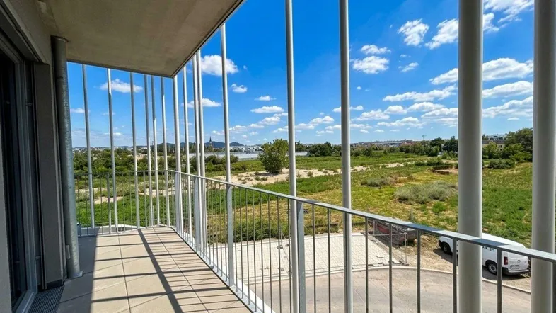 Geräumiger Balkon mit Fliesenboden und weitem Blick über grüne Felder und Wasser.