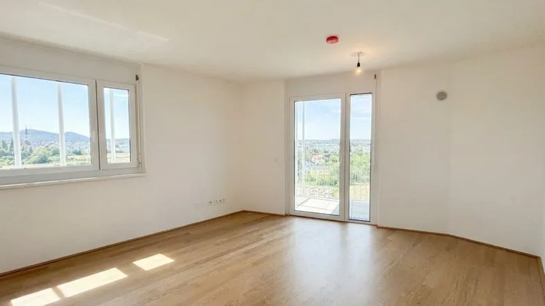 Helles Zimmer mit Holzboden, großen Fenstern und Zugang zu einem Balkon mit Weitblick.