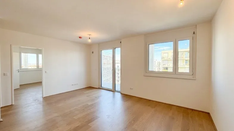 Helles Wohnzimmer mit Parkettboden, großen Fenstern und Zugang zu einem Balkon.