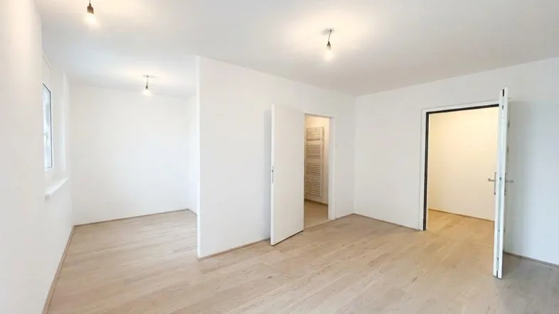 Helles, leeres Zimmer mit hellem Holzboden und weißen Wänden, bereit zur individuellen Gestaltung.