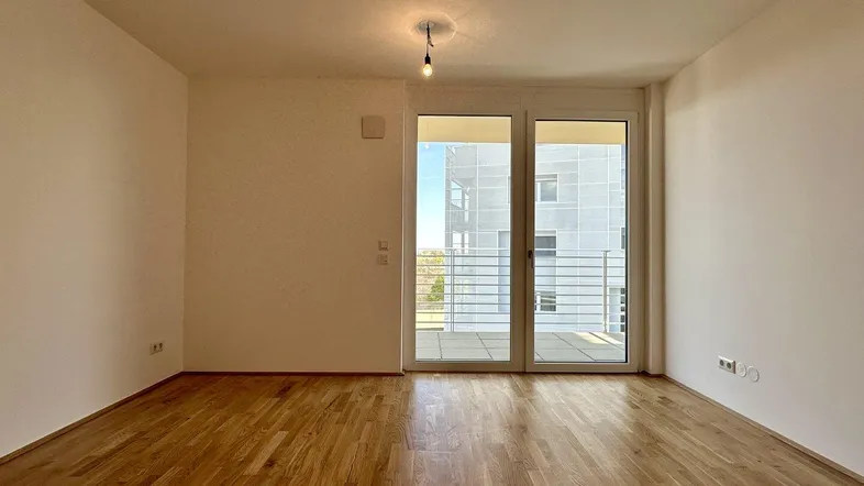 Helles Zimmer mit Parkettboden und Zugang zu einem Balkon, bereit zur individuellen Gestaltung.