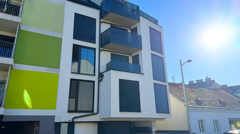Moderne Wohnhausfassade mit Balkonen und großen Fenstern unter strahlendem Sonnenschein.