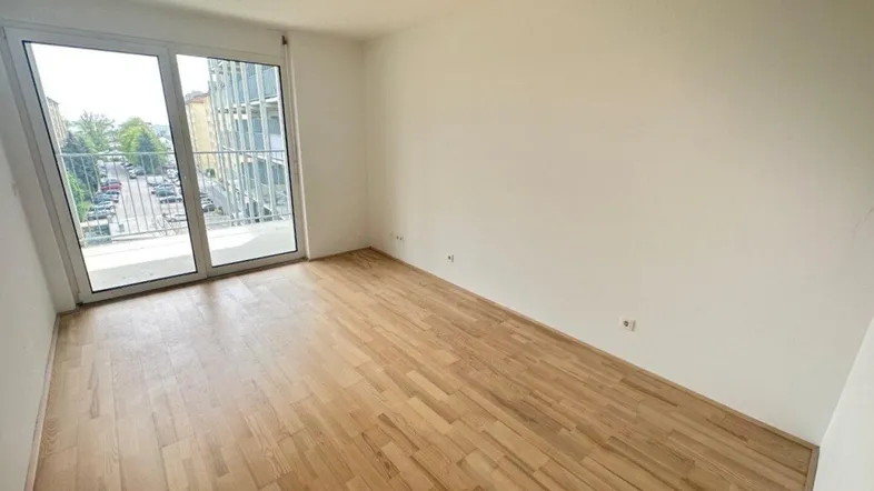 Helles Zimmer mit Holzboden und Zugang zu einem Balkon, bereit zur individuellen Gestaltung.