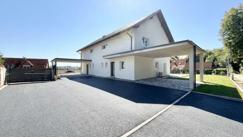 Modernes Einfamilienhaus mit großem Vorplatz und Carport unter strahlend blauem Himmel.