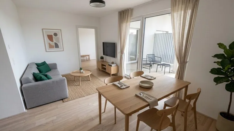 Helles Wohn- und Esszimmer mit Holzboden, moderner Einrichtung und Zugang zu einem Balkon.