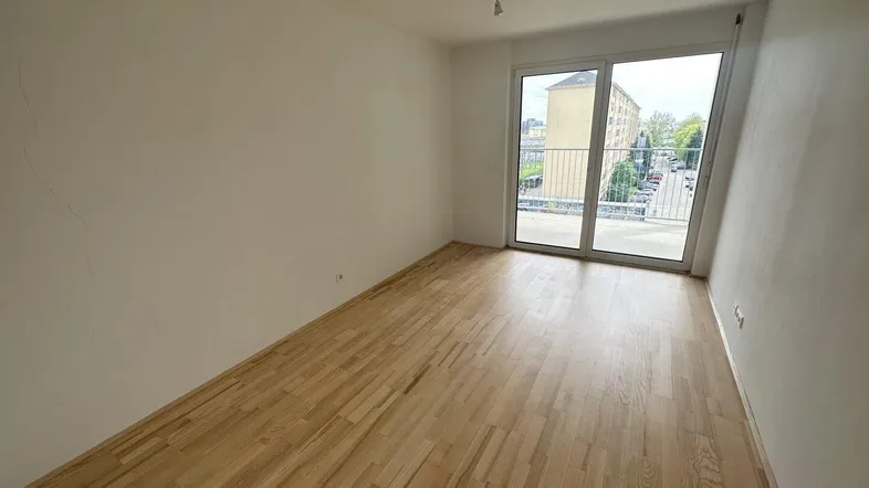 Helles, leeres Zimmer mit Parkettboden und Zugang zu einem französischen Balkon, ideal für individuelle Gestaltung.