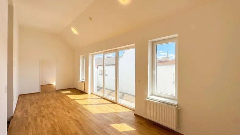 Helles, leeres Wohnzimmer mit Holzboden und Zugang zu einer sonnigen Terrasse.