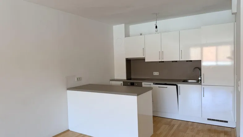 Helle Küche mit weißen Hochglanzschränken, Spülmaschine und einer Kücheninsel mit Arbeitsplatte.